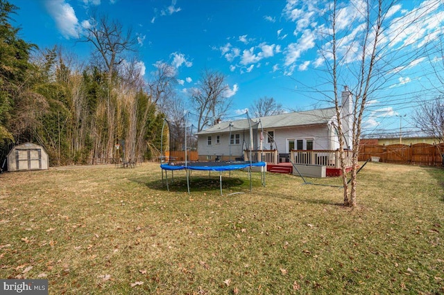 view of yard with an outbuilding, a trampoline, fence, a deck, and a shed