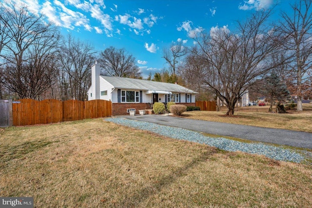 single story home with a chimney, aphalt driveway, fence, a front yard, and brick siding