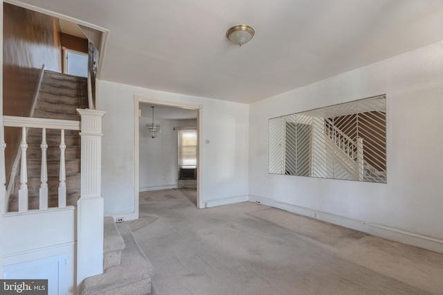 empty room featuring stairs, baseboards, and light colored carpet