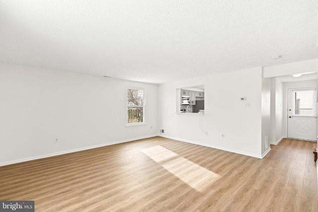 empty room with plenty of natural light, a textured ceiling, and light wood-type flooring