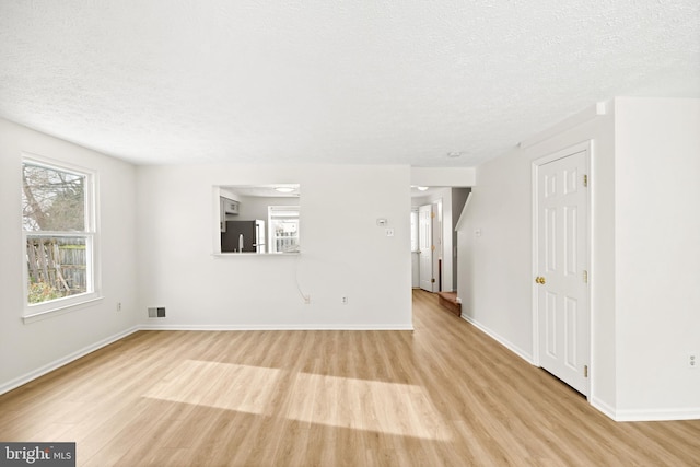 empty room with plenty of natural light, light hardwood / wood-style floors, and a textured ceiling