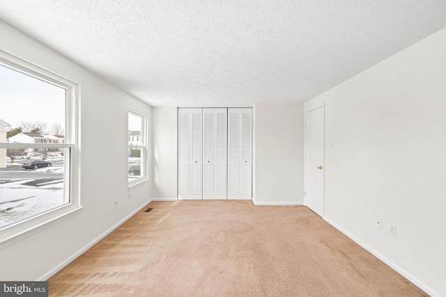 unfurnished bedroom featuring light carpet, a closet, and a textured ceiling