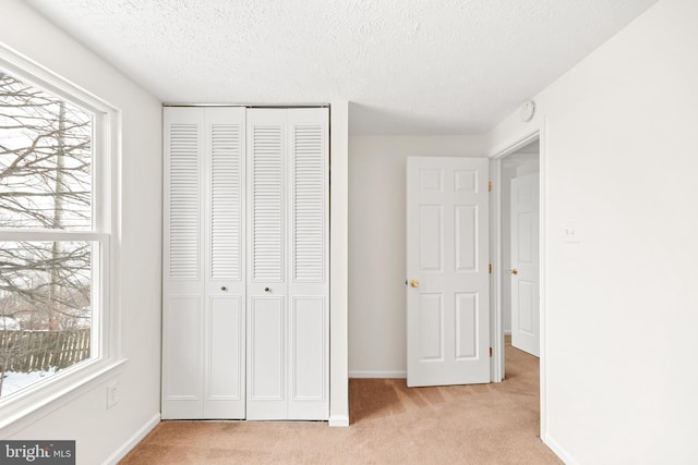 unfurnished bedroom featuring light carpet, a textured ceiling, and a closet