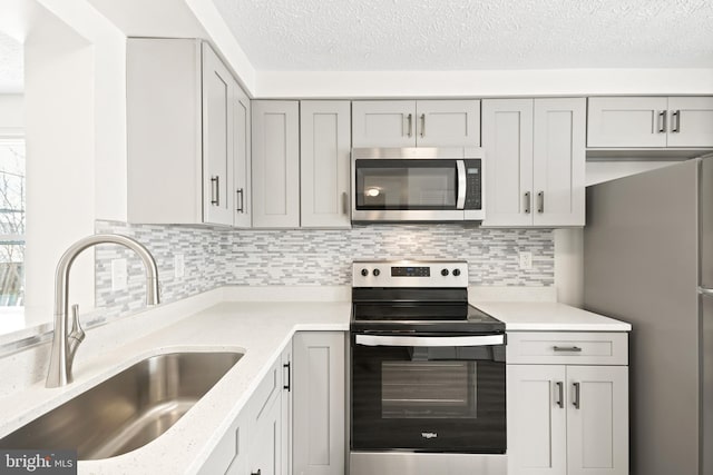 kitchen featuring sink, decorative backsplash, gray cabinets, light stone countertops, and appliances with stainless steel finishes