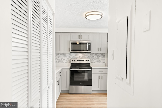 kitchen with gray cabinetry, backsplash, a textured ceiling, appliances with stainless steel finishes, and light hardwood / wood-style floors