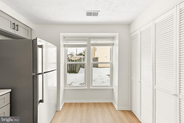 kitchen with stainless steel refrigerator, gray cabinets, light hardwood / wood-style floors, and a textured ceiling