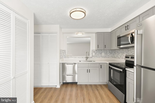 kitchen with decorative backsplash, light wood-type flooring, stainless steel appliances, sink, and gray cabinets