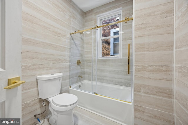 bathroom featuring toilet and bath / shower combo with glass door