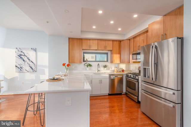 kitchen featuring a kitchen bar, stainless steel appliances, sink, light hardwood / wood-style flooring, and white cabinets