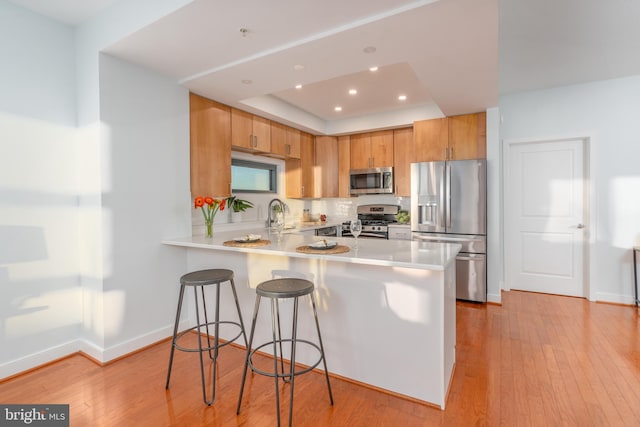 kitchen with a raised ceiling, sink, light wood-type flooring, kitchen peninsula, and stainless steel appliances