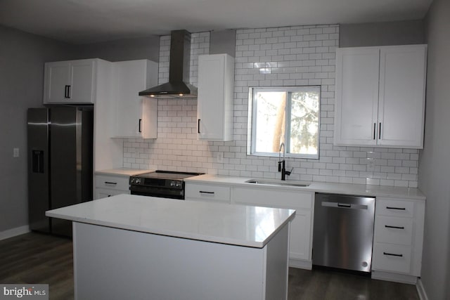 kitchen with stainless steel appliances, a kitchen island, a sink, white cabinets, and wall chimney exhaust hood