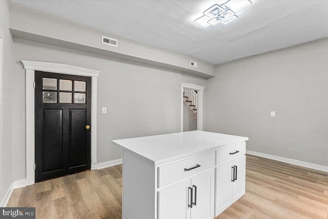 interior space with visible vents, light wood-style flooring, a center island, light countertops, and white cabinetry