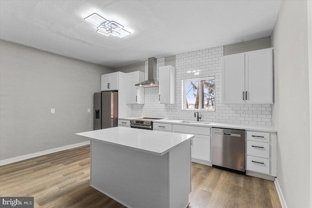 kitchen featuring a center island, stainless steel appliances, light countertops, a sink, and wall chimney exhaust hood