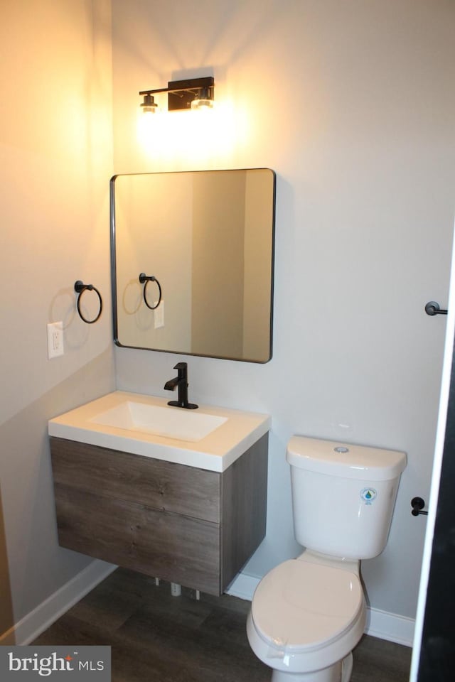 bathroom with toilet, baseboards, wood finished floors, and vanity