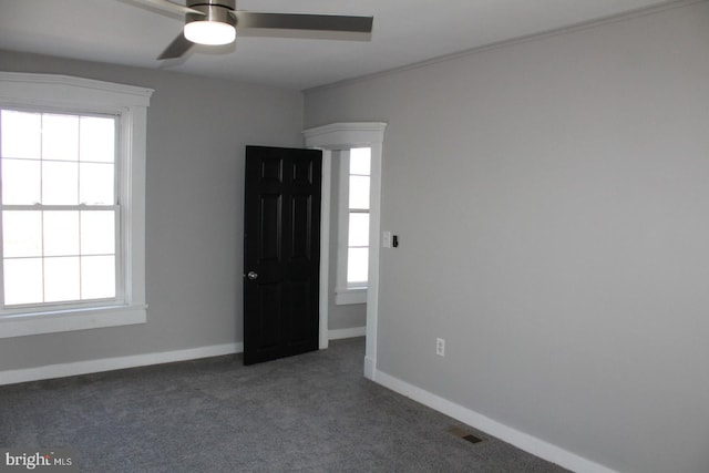 unfurnished bedroom featuring baseboards, multiple windows, dark carpet, and ceiling fan