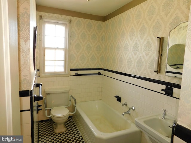 bathroom with tile walls, a bath, sink, and toilet