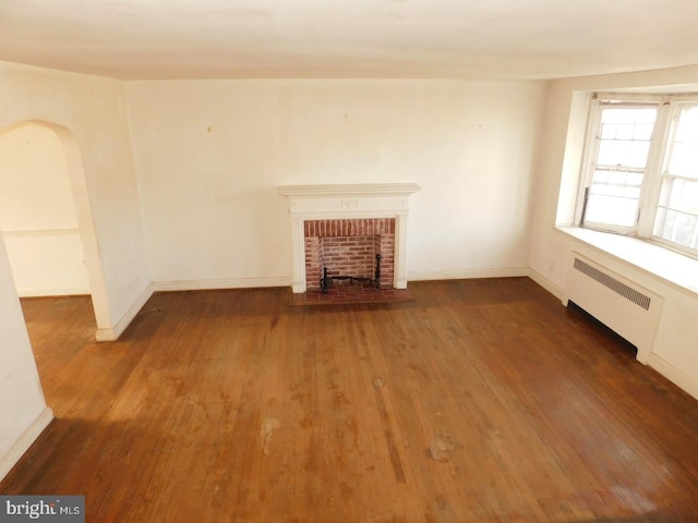 unfurnished living room featuring dark hardwood / wood-style flooring, radiator, and a fireplace