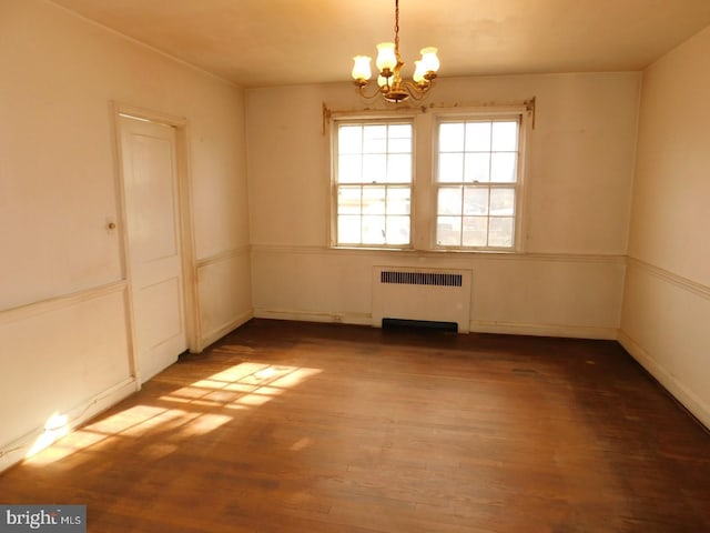 spare room featuring hardwood / wood-style floors, radiator heating unit, and a chandelier