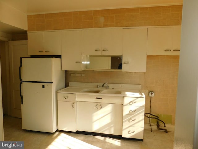 kitchen with white fridge, sink, tile walls, and white cabinets