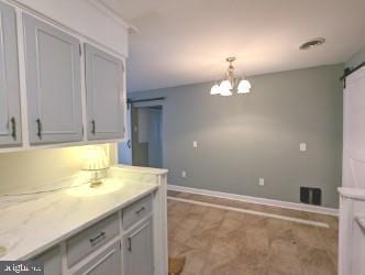 kitchen featuring a barn door, decorative light fixtures, light stone counters, and a notable chandelier