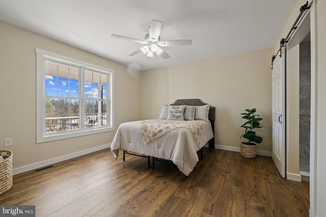 bedroom with dark hardwood / wood-style floors, ceiling fan, and a barn door