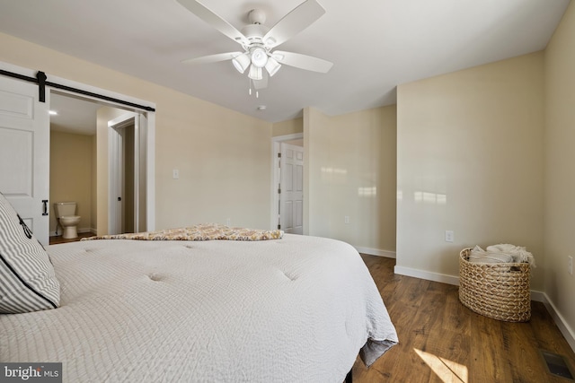 bedroom featuring ceiling fan, ensuite bath, a barn door, and dark hardwood / wood-style flooring