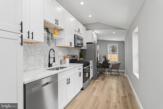 kitchen featuring appliances with stainless steel finishes, lofted ceiling, white cabinetry, decorative backsplash, and sink