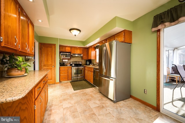 kitchen featuring decorative backsplash, light stone counters, sink, and appliances with stainless steel finishes