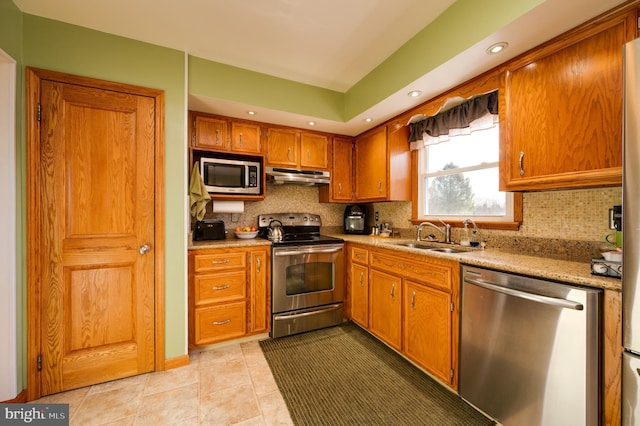 kitchen with appliances with stainless steel finishes, tasteful backsplash, light stone counters, sink, and light tile patterned floors