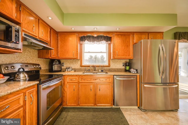 kitchen featuring light stone countertops, backsplash, stainless steel appliances, and sink