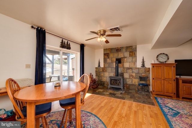 dining area with a wood stove, ceiling fan, and hardwood / wood-style flooring