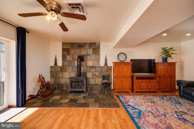 living room with a wood stove, ceiling fan, and wood-type flooring