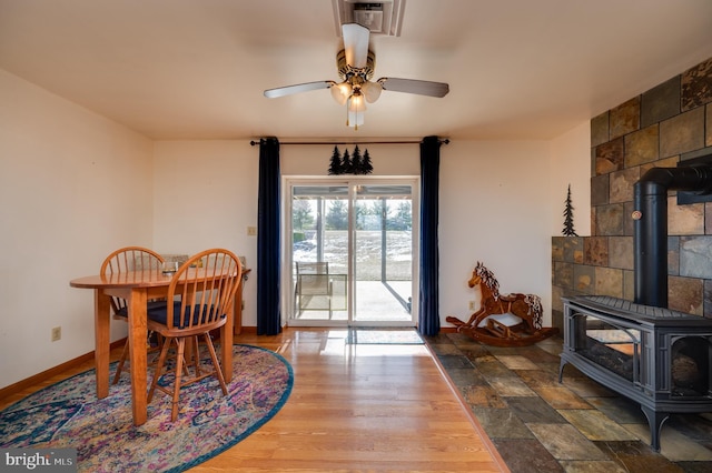 dining room with wood-type flooring, a wood stove, and ceiling fan