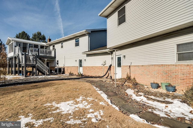 snow covered back of property with cooling unit and a sunroom