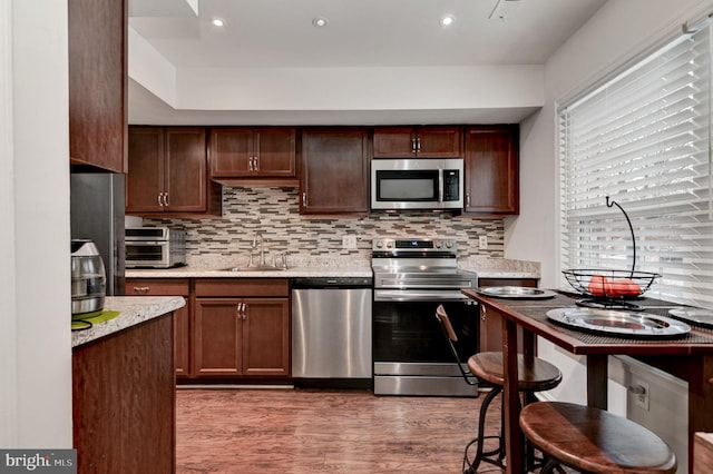 kitchen with tasteful backsplash, sink, dark wood-type flooring, light stone countertops, and appliances with stainless steel finishes