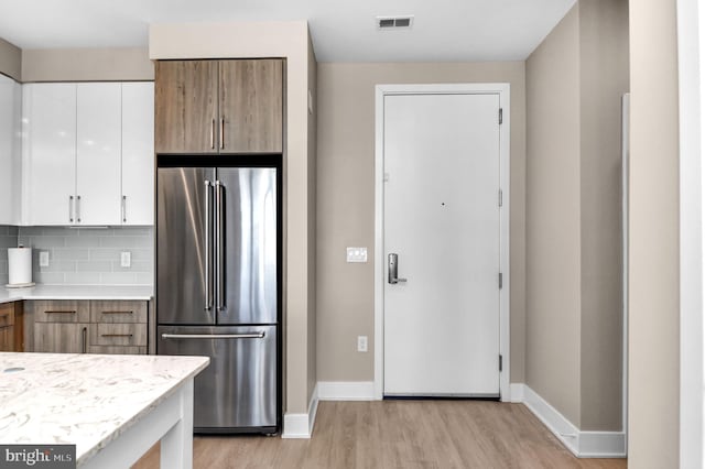 kitchen with light wood-type flooring, high end refrigerator, backsplash, and white cabinetry