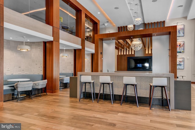 kitchen with pendant lighting, a breakfast bar, light hardwood / wood-style floors, and a towering ceiling