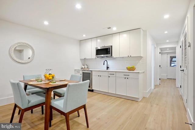 kitchen with white cabinetry, sink, beverage cooler, tasteful backsplash, and light wood-type flooring