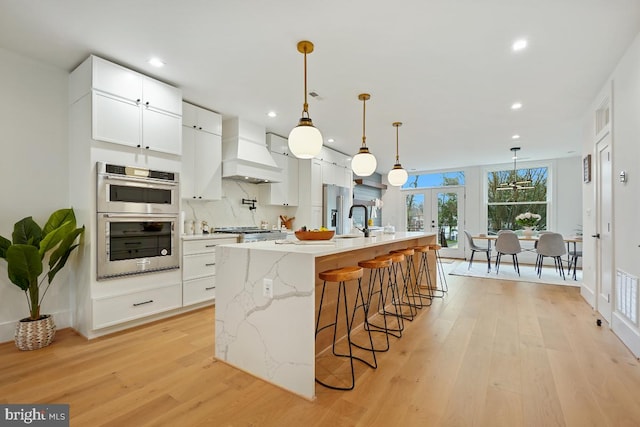 kitchen featuring white cabinets, custom range hood, a kitchen island with sink, and appliances with stainless steel finishes