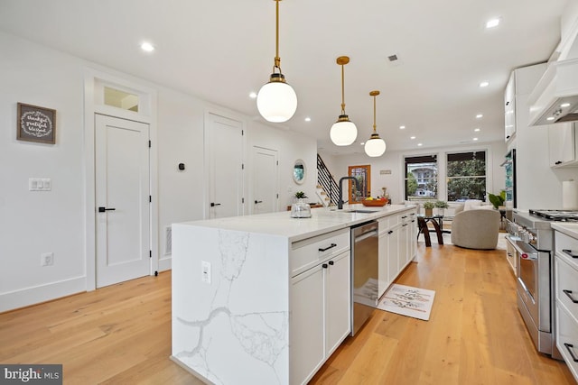 kitchen with sink, hanging light fixtures, stainless steel appliances, an island with sink, and white cabinets