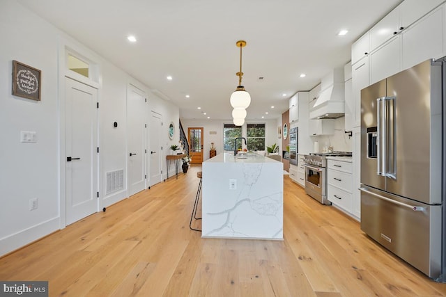 kitchen featuring a center island with sink, white cabinetry, high end appliances, and premium range hood