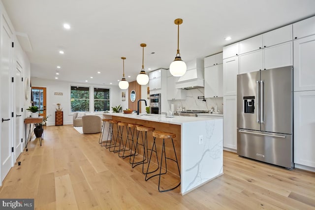 kitchen with a center island with sink, white cabinets, stainless steel appliances, and decorative light fixtures