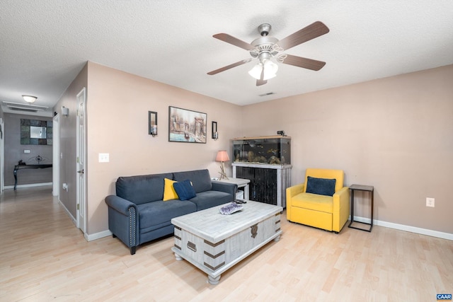 living room featuring ceiling fan, light wood-type flooring, and a textured ceiling