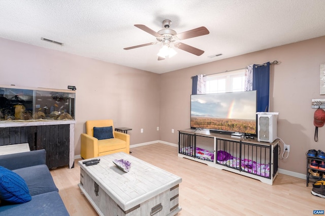 living room featuring ceiling fan, light hardwood / wood-style floors, and a textured ceiling