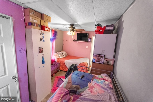 bedroom featuring a drop ceiling, white fridge, and ceiling fan