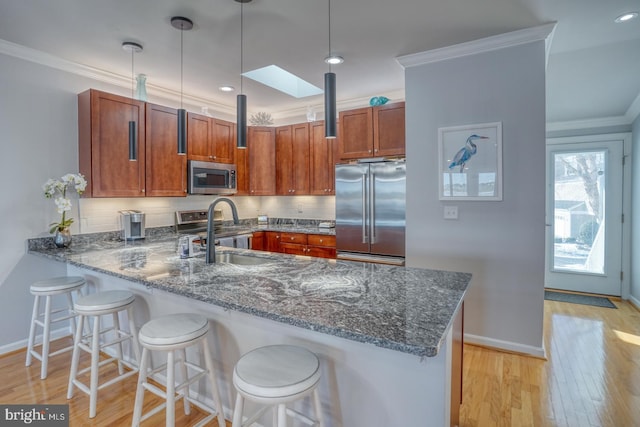 kitchen with kitchen peninsula, pendant lighting, appliances with stainless steel finishes, sink, and a breakfast bar area