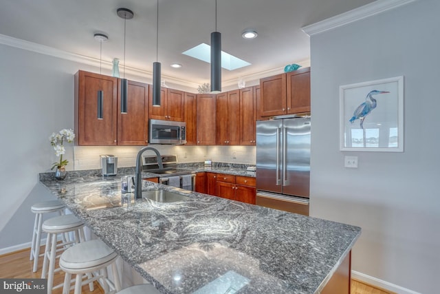 kitchen featuring pendant lighting, appliances with stainless steel finishes, a skylight, sink, and kitchen peninsula