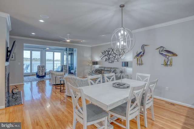 dining space featuring ceiling fan with notable chandelier, a high end fireplace, light hardwood / wood-style flooring, and ornamental molding