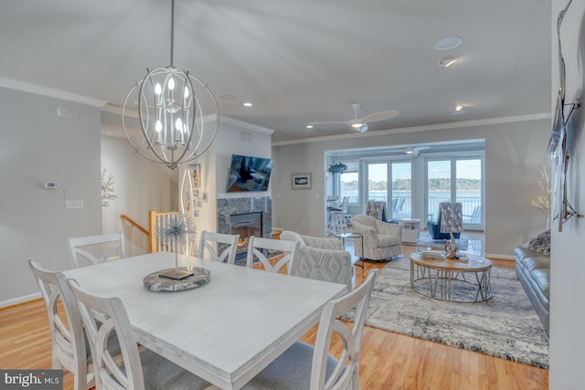 dining area featuring a fireplace, a chandelier, light hardwood / wood-style flooring, and crown molding