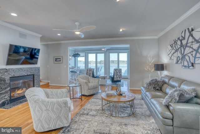 living room featuring ceiling fan, a high end fireplace, crown molding, and wood-type flooring